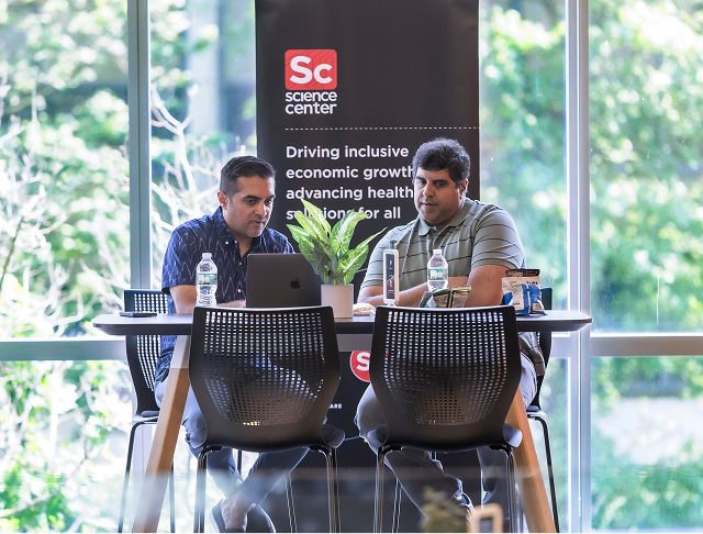 Two professional men look at computer together with backdrop of Science Center panel